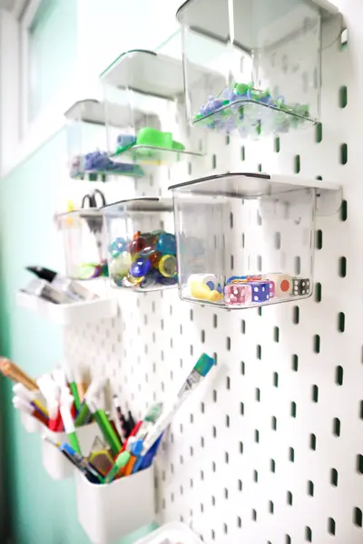 Nahaufname eines Lochbrettes mit Kisten und Kästchen mit therapeutischen Zubehör wie Würfel, Stifte, Murmeln.