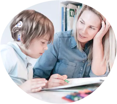 Ein Junge mit Cochlea-Implantat sitzt mit einer Therapeutin vor einem Buch und übt