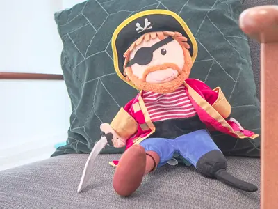 Nahaufname eines Kuscheltier-Piraten mit Augenklappe, Piratenhut, Degen, der auf einem Wartesessel sitzt und in die Kamera lächelt.