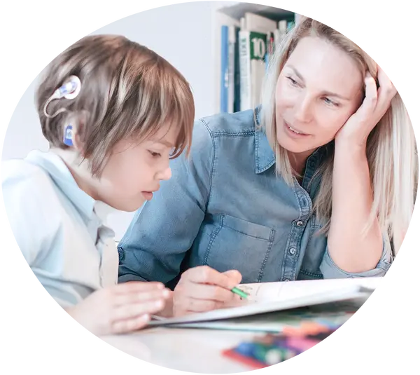 Ein Junge mit Cochlea-Implantat sitzt mit einer Therapeutin vor einem Buch und übt