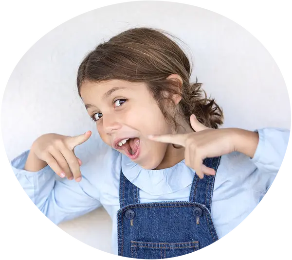 Mädchen in hellblauem Oberteil und Latzhose aus Jeans macht eine freche Pose mit Ihren Händen und hat den Mund geöffnet als würde SIe einen Laut von sich geben